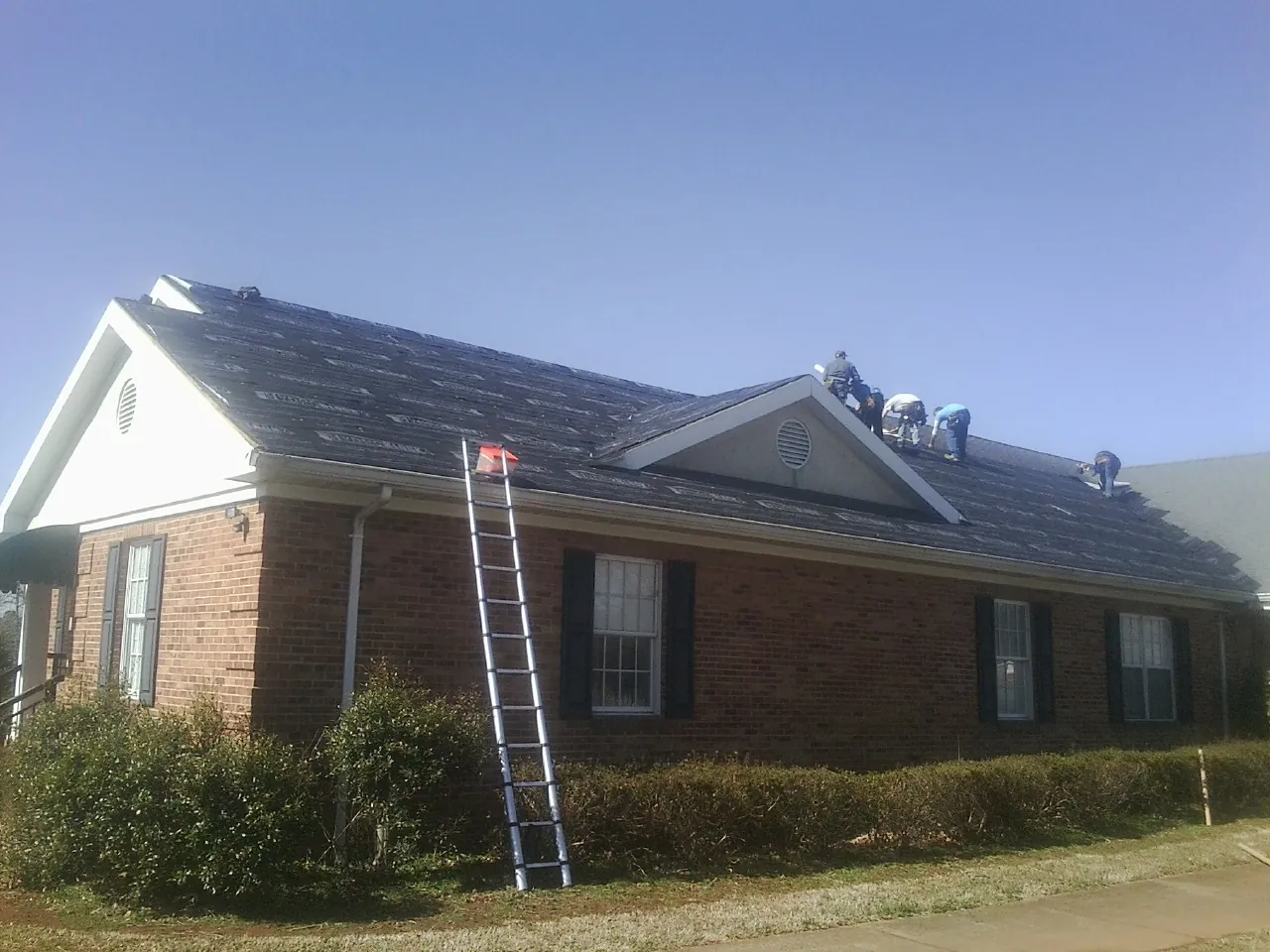 Crew tearing shingles off a brick ranch roof with a ladder set — Metal Roof Repair work by our crew in Solway
