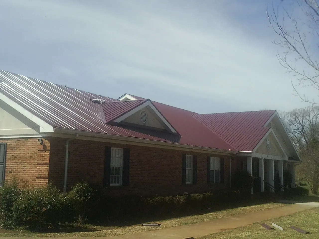 Red metal roof with gabled entries on a long brick building, from a Hail Damage Roof Repair job in Solway
