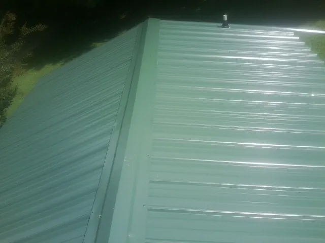 New green metal panels meeting at the ridge of a roof — Flat Roof Repair work by our crew in Solway