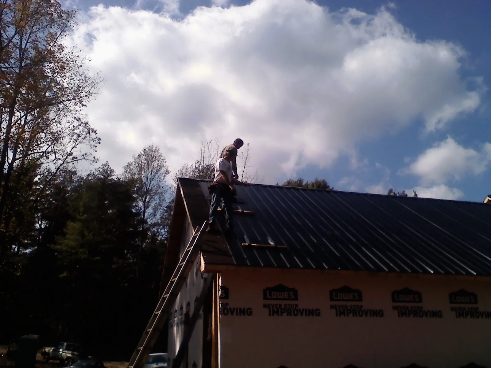 Roofer fastening dark metal panels high against a cloudy sky, from a Roof Inspection job in Solway