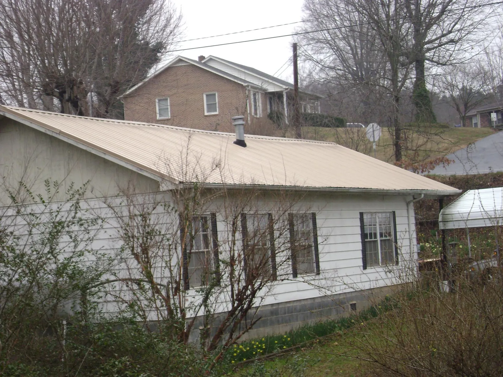 Tan metal roof on a white sided house set into a hillside — Commercial Roofing by Roofing Brothers in Solway